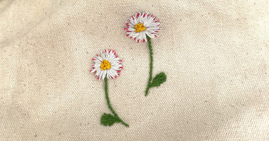 Two embroidered commond daisies on plain linen