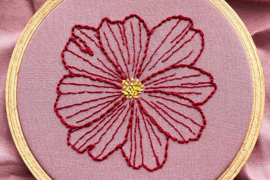 Outline of a red cosmos flower embroidered on rose-pink cotton