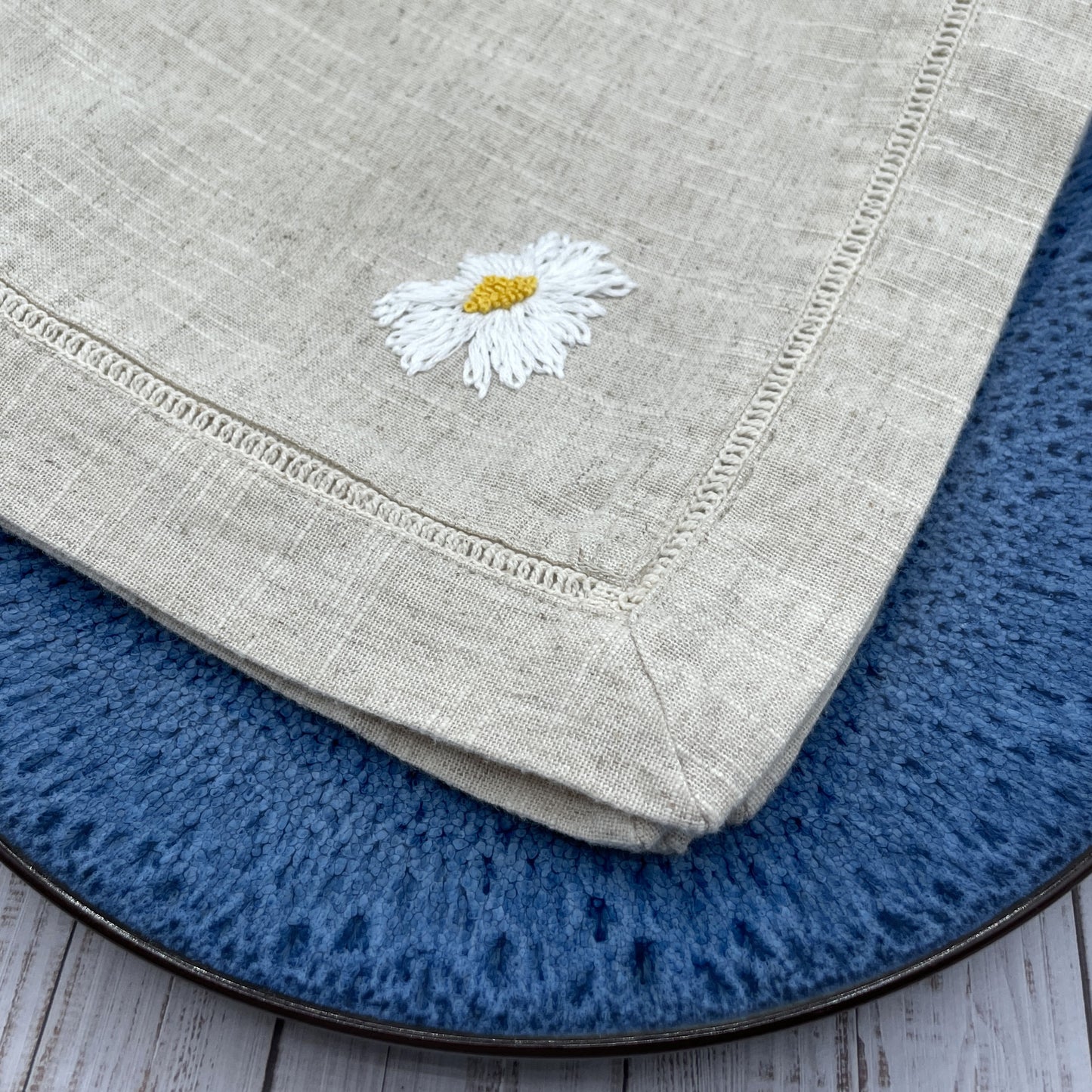 Ox eye daisy flower head embroidered on a linen napkin.