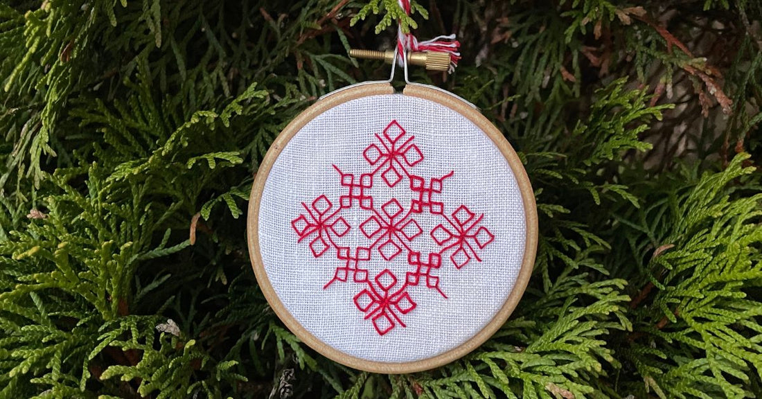 Geometric snowflake embroidered in red thread on white linen.