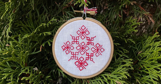 Geometric snowflake embroidered in red thread on white linen.