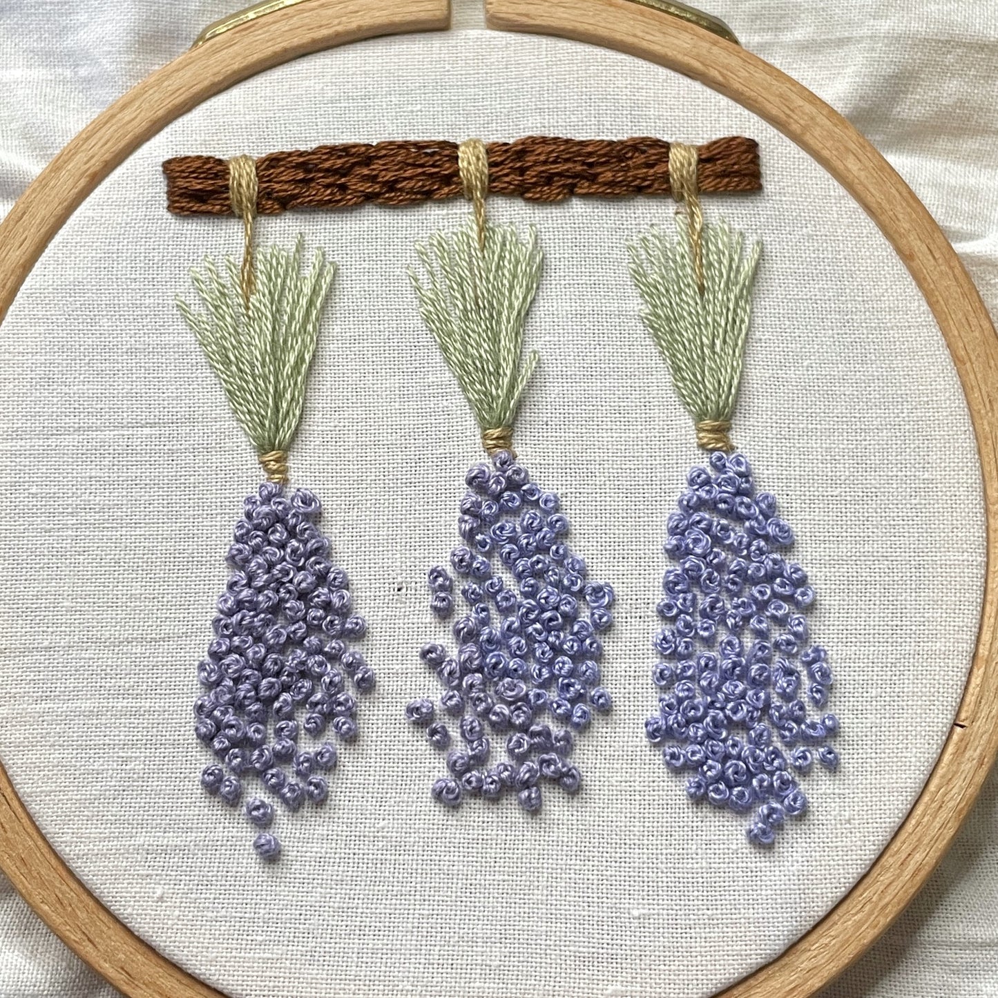 Three embroidered bunches of dried lavender hanging from a beam.