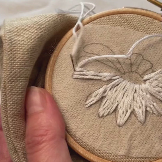 Video of ox eye daisy flower head being hand embroidered on a plain linen pencil case