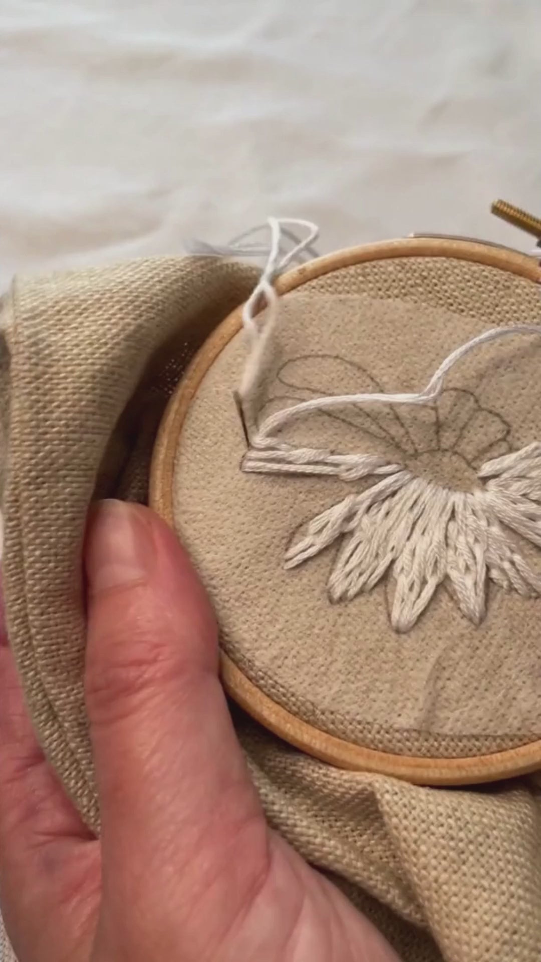 Video of ox eye daisy flower head being hand embroidered on a plain linen pencil case